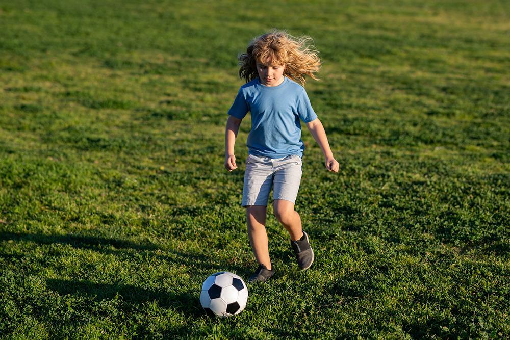 Soccer kid. Kids play football on summer stadium field. Little child boy kicking ball. Little boy shooting at goal, kid kicking football ball